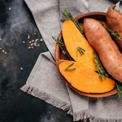 Pomarańczowy batat, pokrojony i w całości, z gałązkami rozmarynu i tymianku, na glinianej misce.