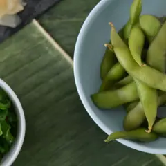 Miseczka z zieloną fasolką edamame, obok sałatka z wodorostów i plasterki imbiru na liściu bananowca.