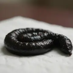 Ciemna kupa uformowana w spiralę, leżąca na białej serwetce. Wygląda jak ciemna, błyszcząca masa z drobnymi czerwonymi drobinkami.