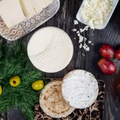 Różne rodzaje sera podpuszczkowego, oliwki, winogrona i koperek na drewnianym stole.