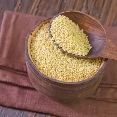 Drewniana miska pełna kaszy jaglanej, z drewnianą łyżką. Czy kasza jaglana ma gluten? Nie, jest bezglutenowa!