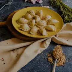 Talerz żółtych pierogów ruskich, posypanych papryką. Obok łyżka kaszy gryczanej i przyprawy. Zastanawiasz się nad pierogi ruskie kcal?