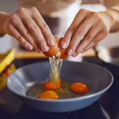 Ręce rozbijają jajko do miski, by sprawdzić, ile białka ma jajko.