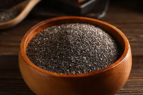 Nasiona chia jak jeść? W drewnianej misce pełnej drobnych, czarnych ziarenek. Idealne do dodania do jogurtu, owsianki czy smoothie.