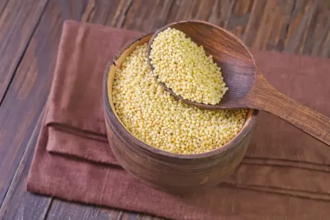 Drewniana miska pełna kaszy jaglanej, z drewnianą łyżką. Czy kasza jaglana ma gluten? Nie, jest bezglutenowa!