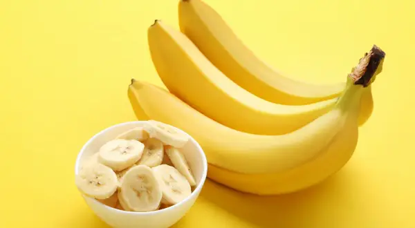 Kilka żółtych bananów i miseczka pokrojonych plasterków. Czy banan jest lekkostrawny? Tak, jest to owoc łatwo przyswajalny.