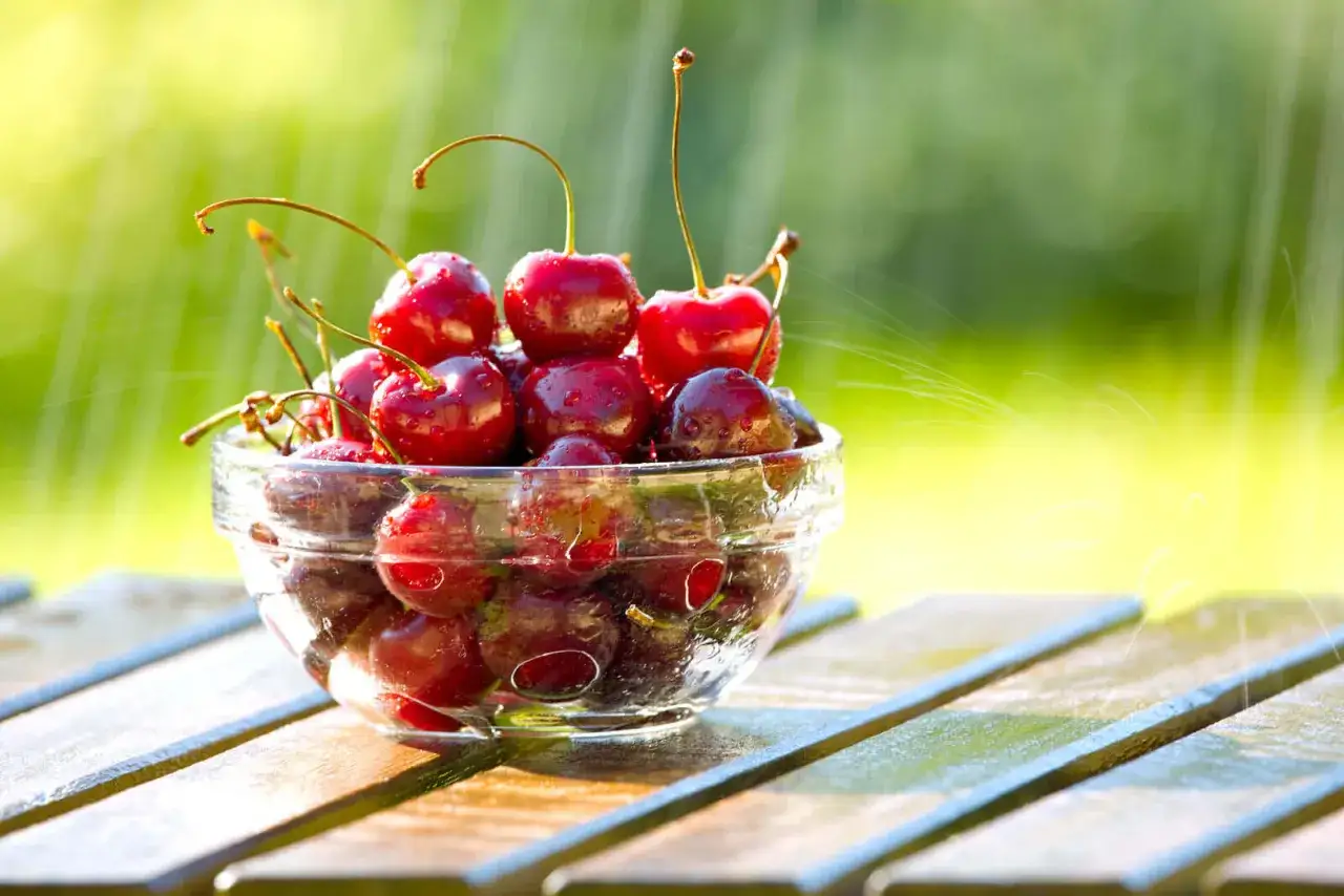 Szklana miseczka pełna soczystych czereśni, z kroplami wody i zielonym tłem. Idealna przekąska, która dostarcza witamin i niewiele czereśnie kcal.