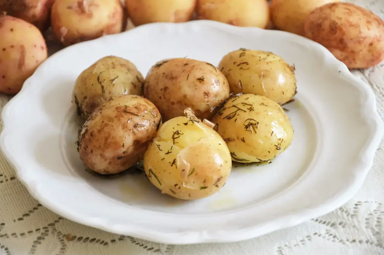Na białym talerzu ułożone są aromatyczne, młode ziemniaki z ziołami.