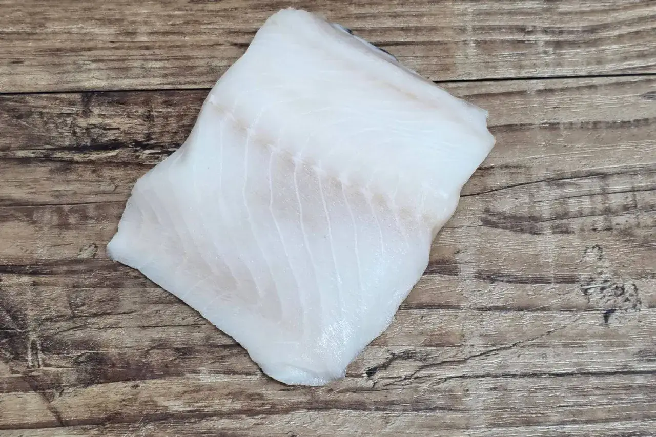 Świeży filet z dorsza czarnego, biały i delikatny, leży na drewnianym blacie.