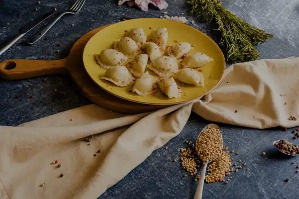 Talerz żółtych pierogów ruskich, posypanych papryką. Obok łyżka kaszy gryczanej i przyprawy. Zastanawiasz się nad pierogi ruskie kcal?