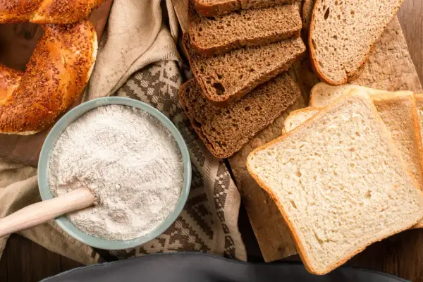 Mąka, chleb i bajgiel – oto główne źródła, w czym jest gluten. Składniki do wypieku na drewnianej desce.